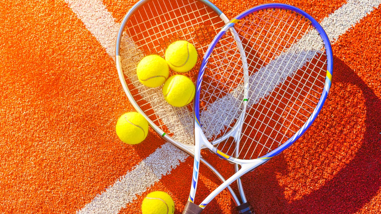 Flat lay of two tennis rackets and tennis balls on a clay tennis court